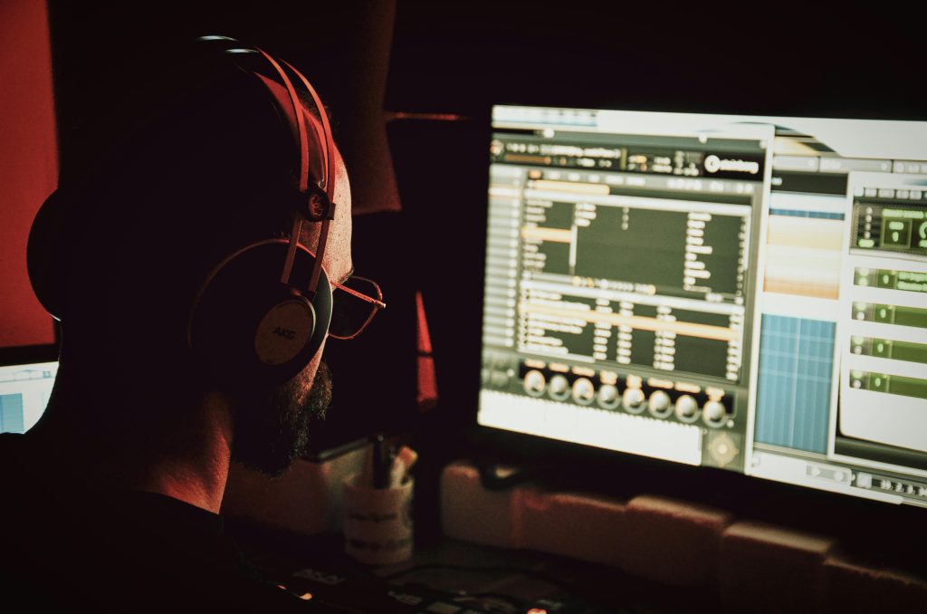 A music producer working in a studio, focused on a computer screen displaying digital production software.