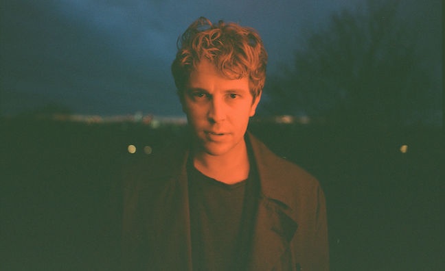 Singer-songwriter Tom Odell photographed outdoors at dusk, wearing a dark coat.